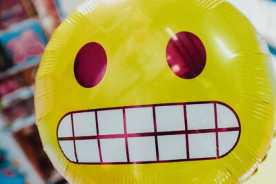 Yellow balloon face with wide eyes and wide smile showing teeth in a scary grimace